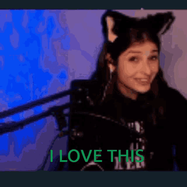 a woman wearing cat ears is smiling in front of a microphone and says i love this .