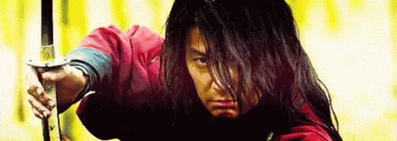 a man with long hair is holding a sword and pointing it at the camera .