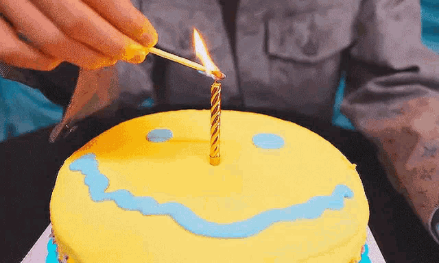 a person is lighting a candle on a yellow birthday cake .