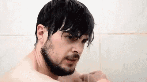 a shirtless man with a beard is taking a shower in a bathroom .