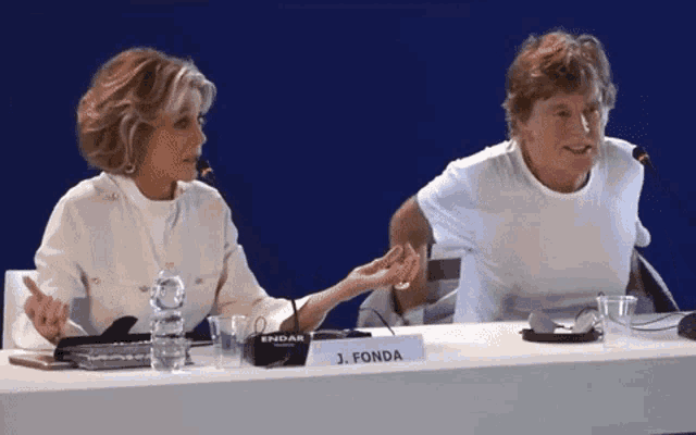 two people sitting at a table with a sign that says j fonda
