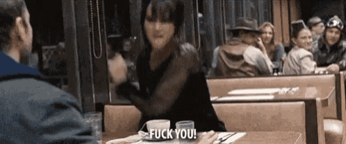 a man and a woman are sitting at a table in a diner and the woman is saying `` fuck you '' .