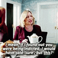 a woman is sitting at a table with a teapot and a cat and talking to another woman .