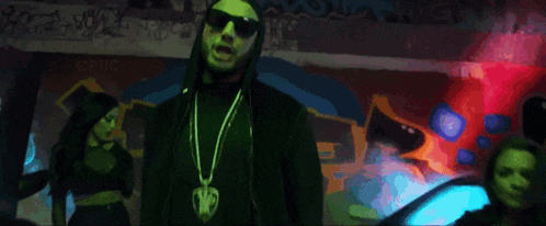 a man wearing a hoodie and sunglasses is standing in front of a wall that says optic on it