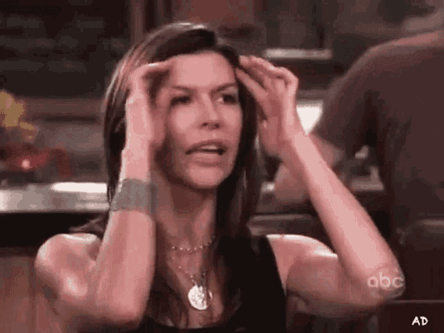 a woman in a black tank top is holding her head and making a funny face .