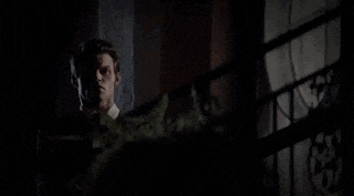a man in a suit and tie is standing on a balcony at night looking out the window .