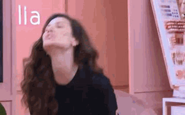 a woman with long hair is making a funny face while sitting in front of a pink wall .