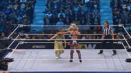 two women are wrestling in a wrestling ring with a referee standing behind them .
