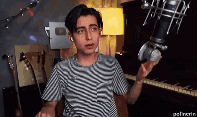 a young man in a striped shirt is singing into a microphone .