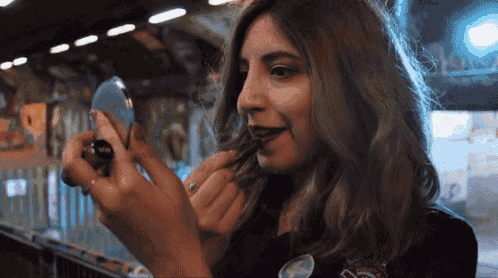 a woman is applying lipstick while looking at herself in a mirror