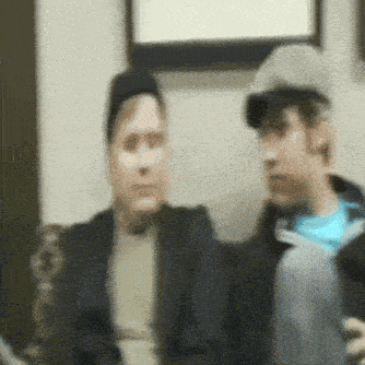 a blurry picture of two men sitting on a couch with one wearing a hat