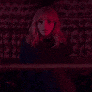 a woman in a black dress is standing in a dark room with red lights behind her .