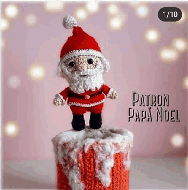 a crocheted santa claus figurine is standing on top of a christmas gift box .