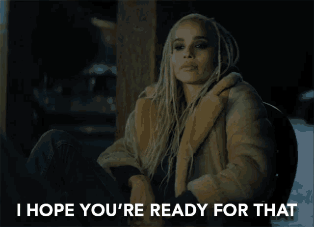 a woman in a fur coat sits next to a sign that says " i hope you 're ready for that "