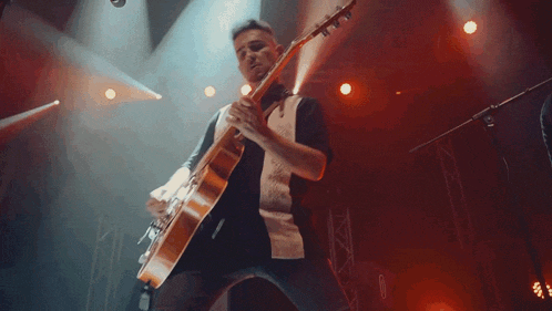 a man is playing a guitar on a stage with red lights behind him