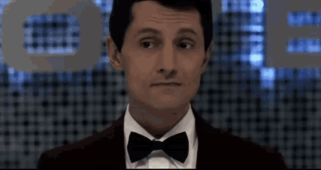a man in a tuxedo with a bow tie looks at the camera