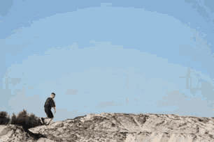a person standing on top of a sandy hill with a blue sky in the background