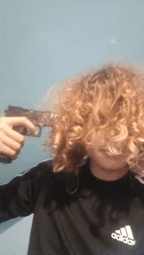 a person with curly hair is holding a gun to their head