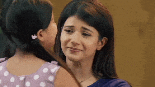 a woman is hugging a little girl who is crying and looking at her .
