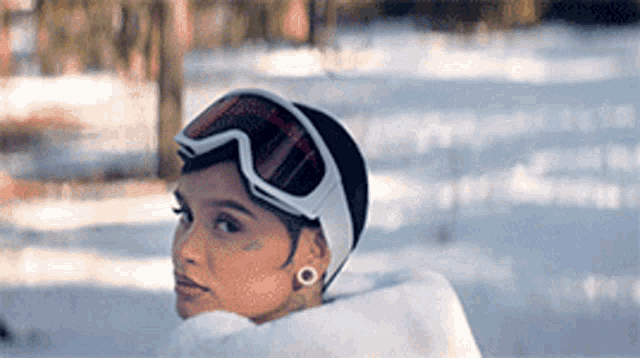 a woman wearing ski goggles and a hat is laying in the snow