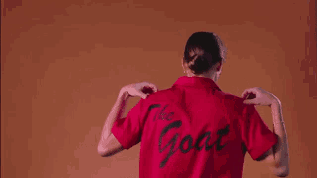 a woman is putting on a red t-shirt with the word goat on the back .