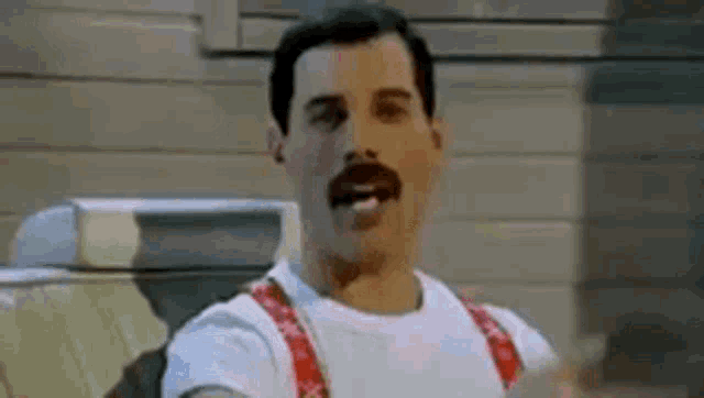 a man with a mustache is smoking a cigarette while wearing suspenders and a white shirt .