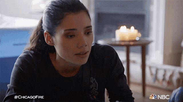 a woman sitting in front of a fireplace with a candle on a table and the hashtag #chicagofire on the bottom
