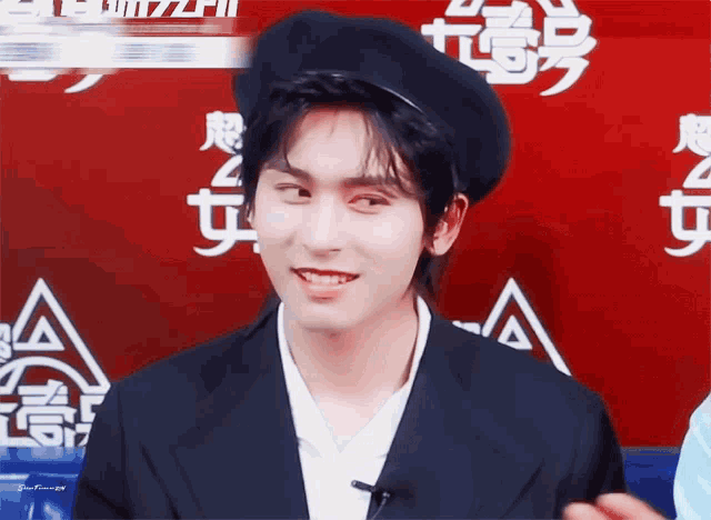 a man wearing a black beret is smiling in front of a red background with chinese writing
