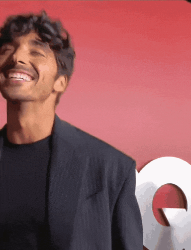 a man in a suit is smiling in front of a gq logo