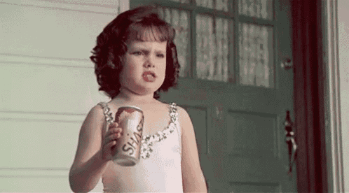 a little girl is holding a can of soda in front of a door .