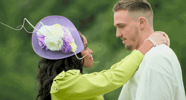 a woman wearing a purple hat and a green jacket is hugging a man
