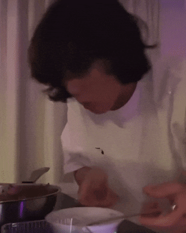 a man in a white shirt is cooking with a spoon in a bowl .