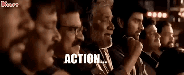 a group of men are sitting in a row and one of them is holding a microphone and says action .
