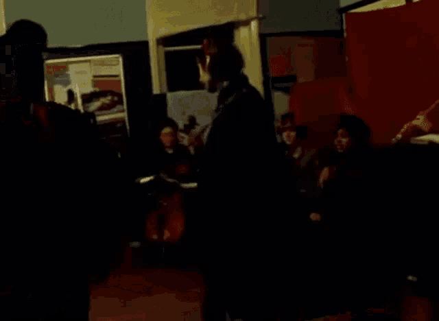 a group of people are gathered in a dark room with a red curtain behind them
