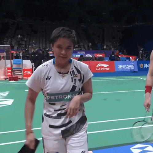 a woman in a petronas shirt holds a racket