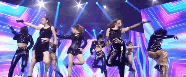 a group of women are dancing on a stage with purple and blue lights
