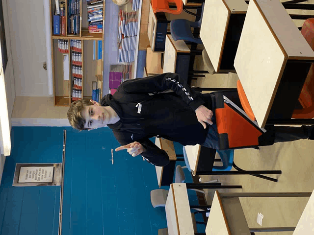 a boy standing in a classroom with a sign on the wall that says ' i 'm not a robot '