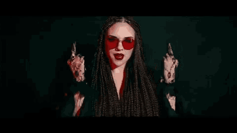 a woman wearing red sunglasses is holding a gun and giving the middle finger .