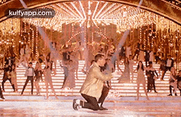 a man is kneeling down on the ice in front of a group of people dancing .