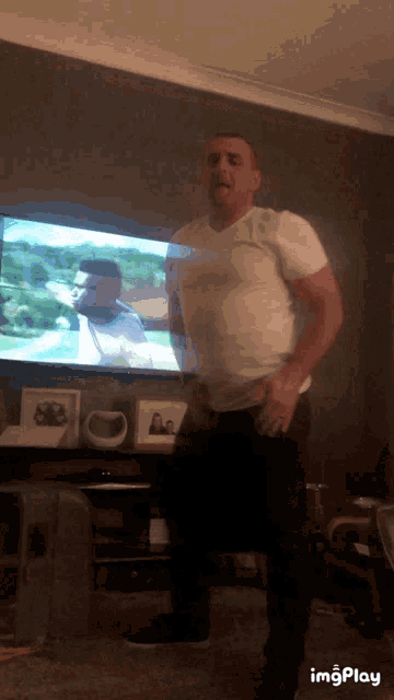 a man in a white shirt is dancing in front of a flat screen television