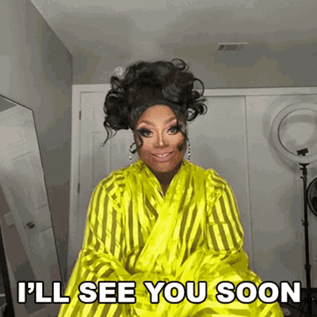 a drag queen is wearing a yellow robe and says i 'll see you soon .