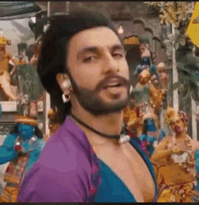 a man with a beard and a purple shirt is standing in front of a group of statues .