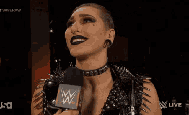 a woman with spikes on her sleeves is talking into a microphone with a wwe logo in the corner