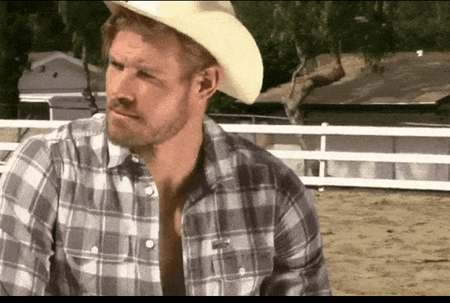 a man wearing a cowboy hat and plaid shirt is standing in front of a white fence