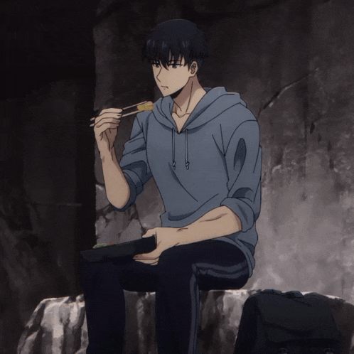 a man in a blue hoodie is sitting on a rock eating something with chopsticks