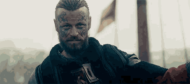 a man with a beard and tattoos on his face is holding a sword in his hand .