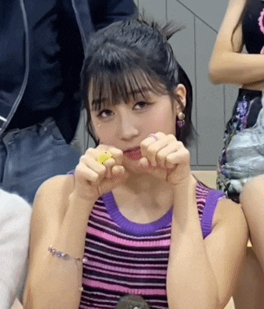 a woman in a purple and pink striped tank top is holding a yellow object in her mouth