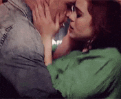 a man and a woman are kissing on a couch . the woman is wearing a green shirt .
