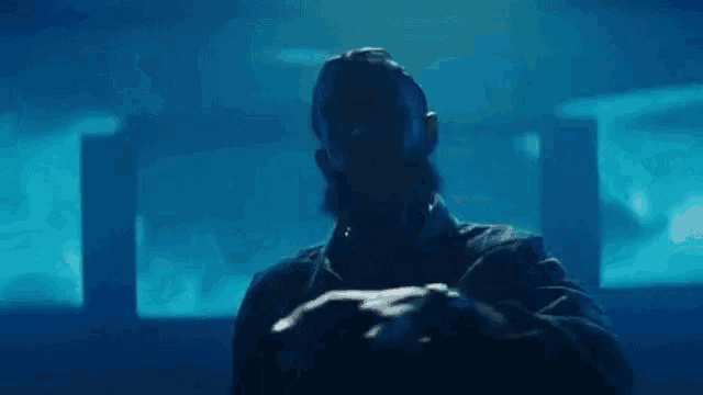 a man with a beard is standing in a dark room with a blue background .