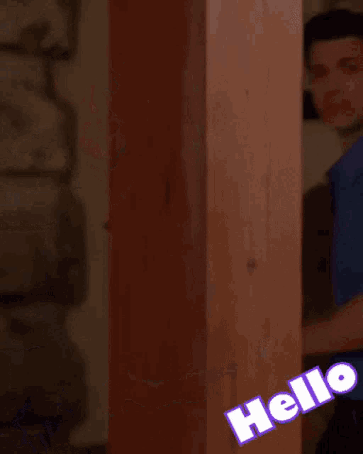 a man in a blue shirt is standing next to a vase of purple flowers and a sign that says hello
